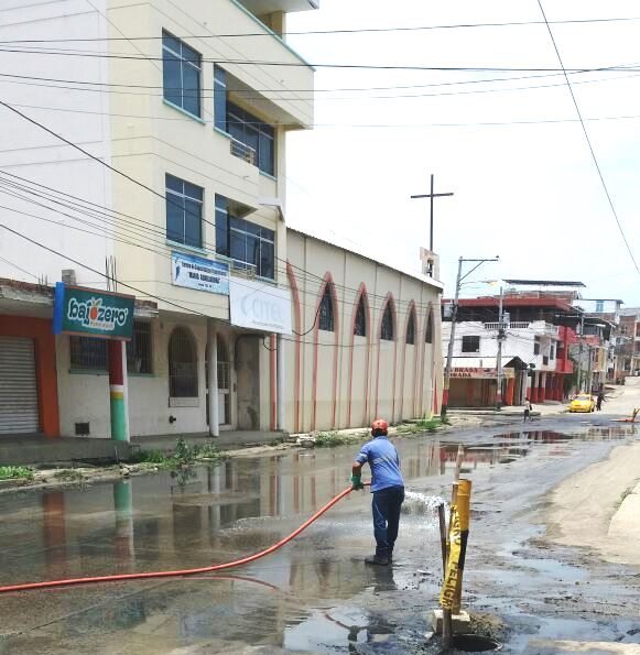Calle de Los Esteros de Manta inundada con agua sucia de alcantarilla. Un obrero de la EPAM arroja agua limpia para descontaminarla. Manabí, Ecuador.
