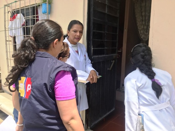 Funcionarias de salud pública, en la puerta de un hogar suministrando información preventiva contra enfermedades virales. Manabí, Ecuador.