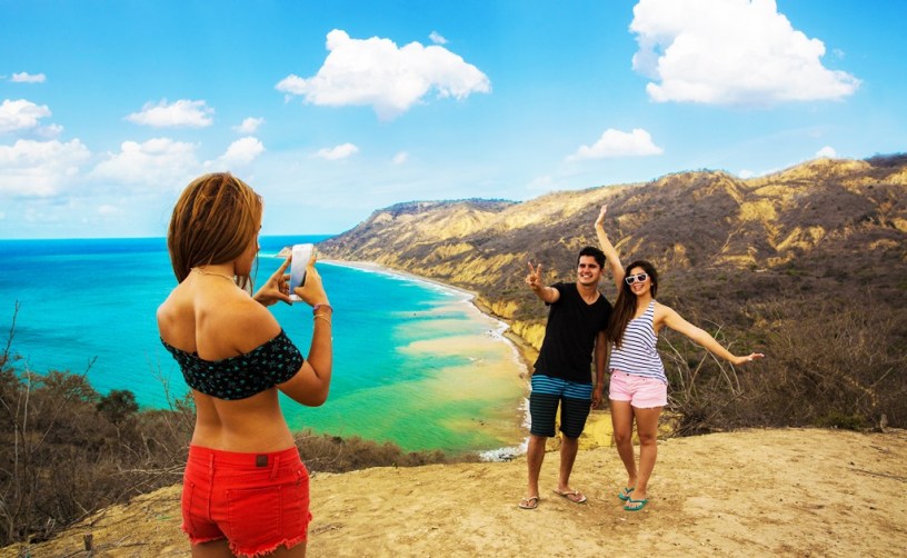 Tres jóvenes turistas hacen fotos en un rincón marino de la zona rural del Cantón Manta. Manabí, Ecuador.